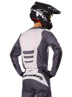 Zawodnik motocrossowy od tyłu w zestawie Alpinestars 2025 Fluid Haul, szaro-biała koszulka i spodnie, czarny kask z białą grafiką, żółte gogle, dopasowany strój wyścigowy