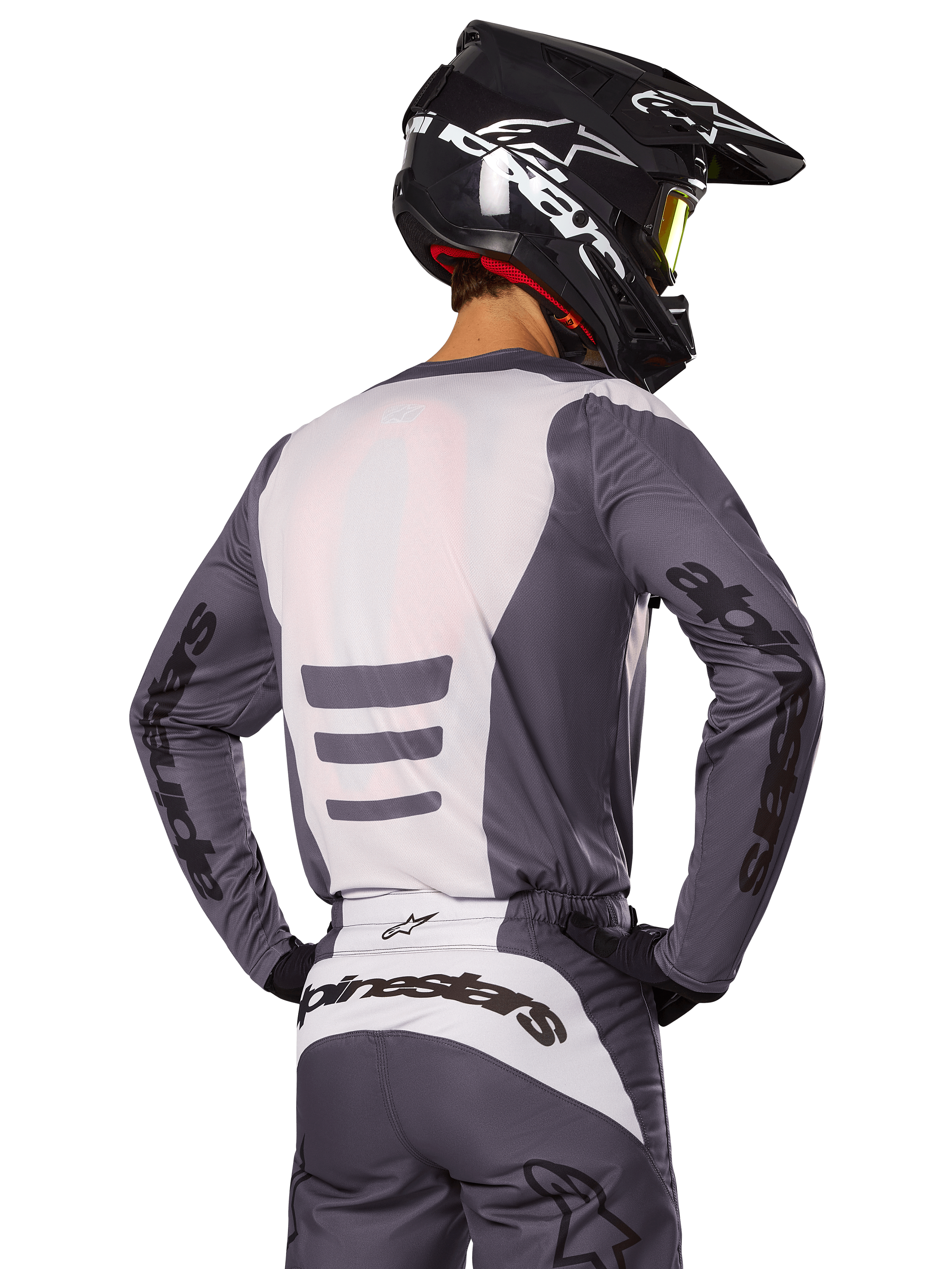 Zawodnik motocrossowy od tyłu w zestawie Alpinestars 2025 Fluid Haul, szaro-biała koszulka i spodnie, czarny kask z białą grafiką, żółte gogle, dopasowany strój wyścigowy