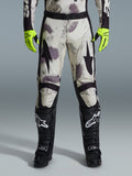 Spodnie Alpinestars 2026 Racer Lahnd, spodnie motocrossowe, wzór Sand Camo z szarymi i fioletowymi abstrakcyjnymi grafikami, widoczne z neonowożółtymi rękawicami i czarnymi butami, czarne logo gwiazdy na udach i czarny pas w talii, wytrzymały sprzęt do wyścigów off-road