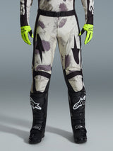 Spodnie Alpinestars 2026 Racer Lahnd, spodnie motocrossowe, wzór Sand Camo z szarymi i fioletowymi abstrakcyjnymi grafikami, widoczne z neonowożółtymi rękawicami i czarnymi butami, czarne logo gwiazdy na udach i czarny pas w talii, wytrzymały sprzęt do wyścigów off-road