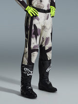 Alpinestars Racer Lahnd Pants 2026, spodnie motocrossowe, Sand Camo, zestawione z neonowożółtymi rękawicami i czarnymi butami motocrossowymi, z abstrakcyjnym wzorem kamuflażu i czarnymi panelami bocznymi, ergonomiczna konstrukcja off-road