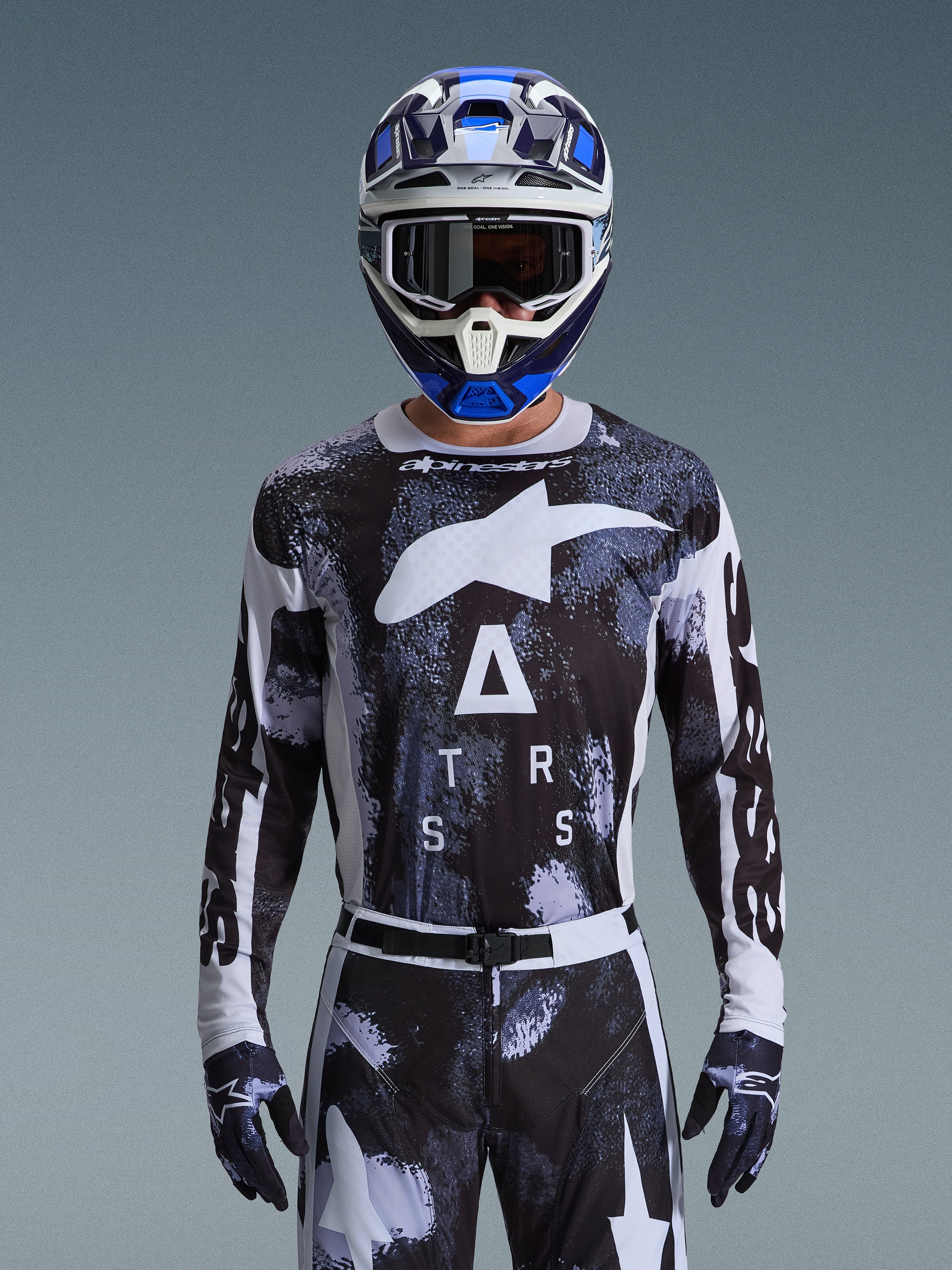 Alpinestars 2026 Racer Lahnd Jersey, bluza motocrossowa, wzór Iron Camo w kolorystyce czarno-białej, z wyraźnym logo gwiazdy i napisem ASTARS, noszona z pasującymi spodniami i niebieskim kaskiem motocrossowym