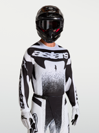 Koszulka Techstar Swan Alpinestars, męska koszulka motocrossowa, czarna i biała, sportowy krój, laserowo wycinana wentylacja, model w kasku i rękawicach.