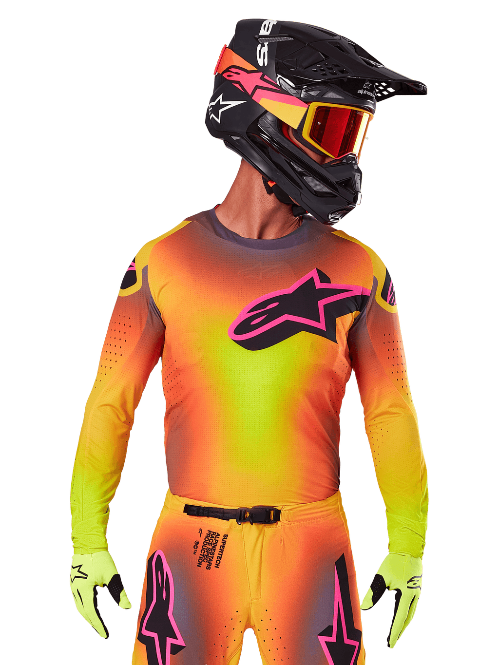 Motocyklista motocrossowy ubrany w koszulkę 2025 Supertech Lipan, jaskrawy gradient kolorów żółtego, pomarańczowego i różowego, duże czarne logo gwiazdy Alpinestars z różową obwódką na piersi, laserowo wycinane perforacje dla wentylacji, sportowy krój wyścigowy, w zestawie z pasującymi spodniami, żółtymi rękawicami i czarnym kaskiem z goglami.