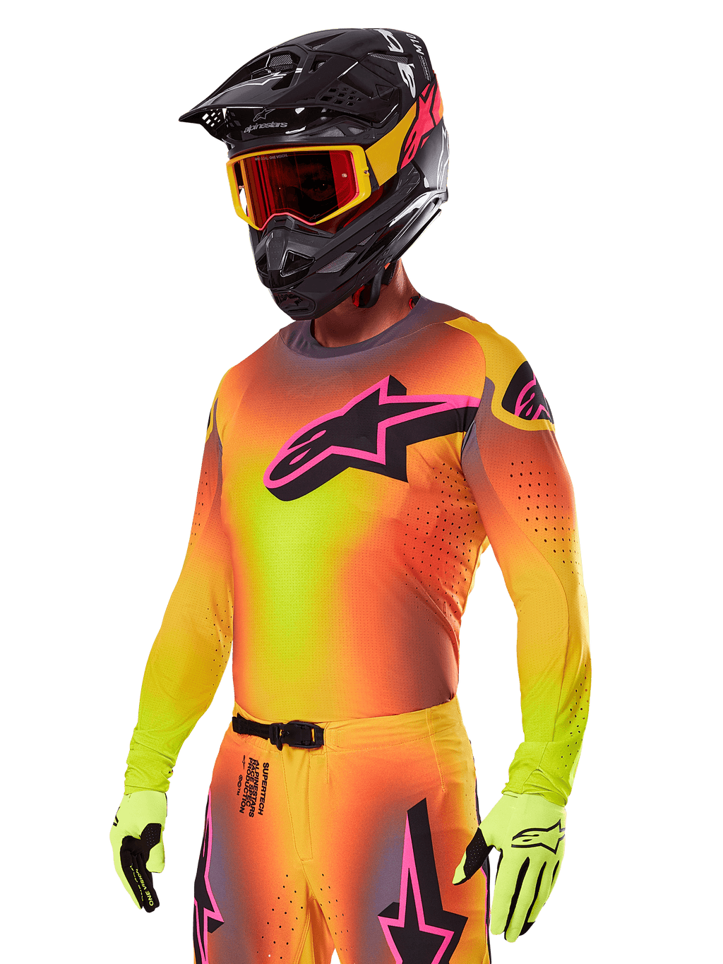 Motocyklista motocrossowy w zestawie Alpinestars 2025 Supertech Lipan, z koszulką z żółto-pomarańczowym gradientem i różowo-czarnym logo Astars, neonowożółtymi rękawicami oraz czarnym kaskiem z czerwonymi goglami, profesjonalna odzież do wyścigów terenowych.