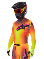 Motocyklista motocrossowy w zestawie Alpinestars 2025 Supertech Lipan, z koszulką z żółto-pomarańczowym gradientem i różowo-czarnym logo Astars, neonowożółtymi rękawicami oraz czarnym kaskiem z czerwonymi goglami, profesjonalna odzież do wyścigów terenowych.