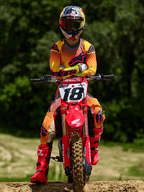 Motocyklista motocrossowy siedzący na czerwonym motocyklu crossowym Honda z numerem startowym 18, ubrany w koszulkę Alpinestars 2025 Supertech Lipan i pasujące spodnie w kolorze żółto-różowym, jaskraworóżowe buty Alpinestars, kask Red Bull, profesjonalny strój wyścigowy do jazdy terenowej.