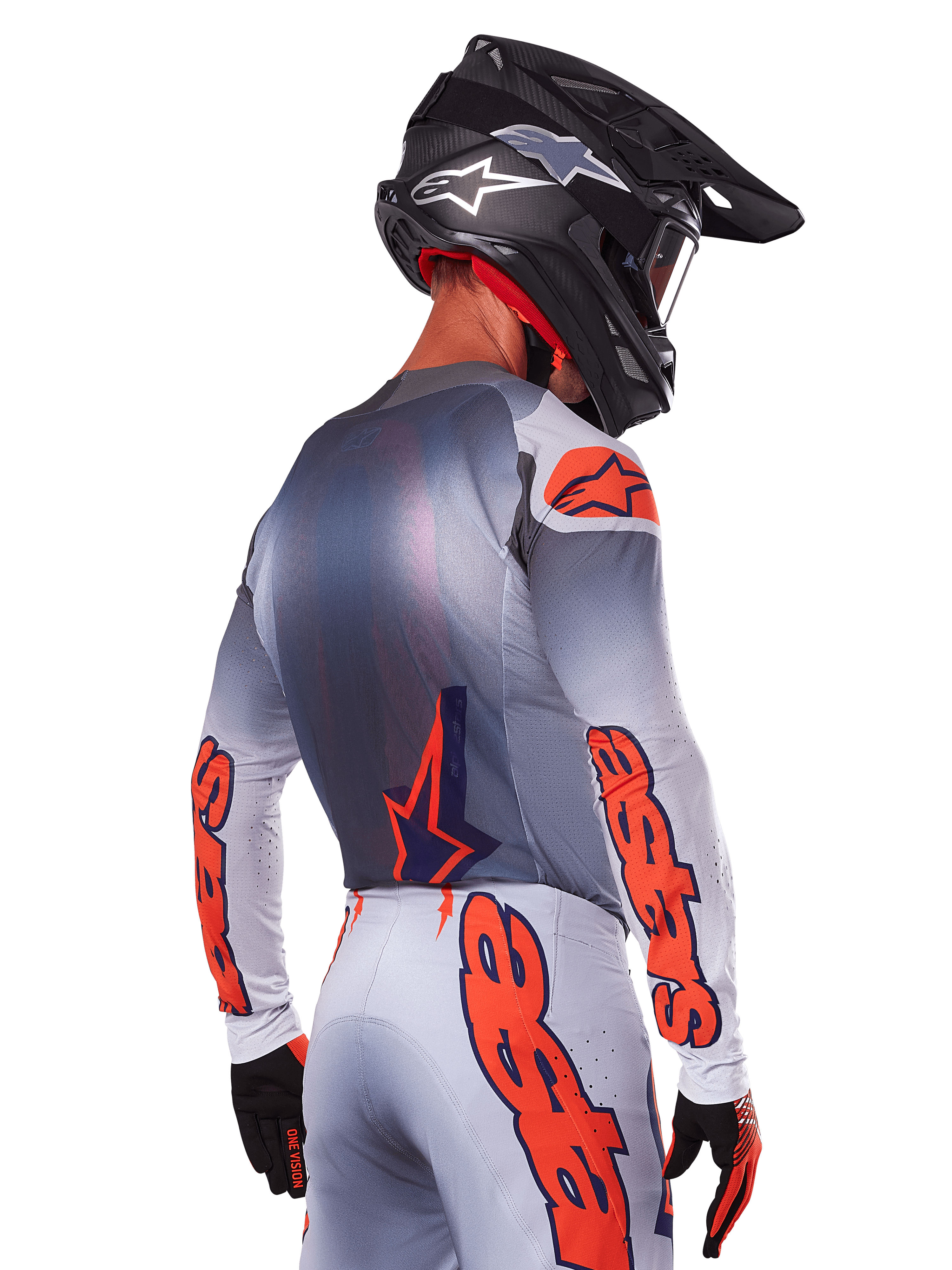 Motocyklista motocrossowy widoczny od tyłu w koszulce Alpinestars 2025 Supertech Lipan w kolorze Gray Orange Fluo, z wyraźnymi pomarańczowymi logotypami na rękawach i plecach, w zestawie z dopasowanymi spodniami i czarnym kaskiem, profesjonalny strój wyścigowy do jazdy w terenie.