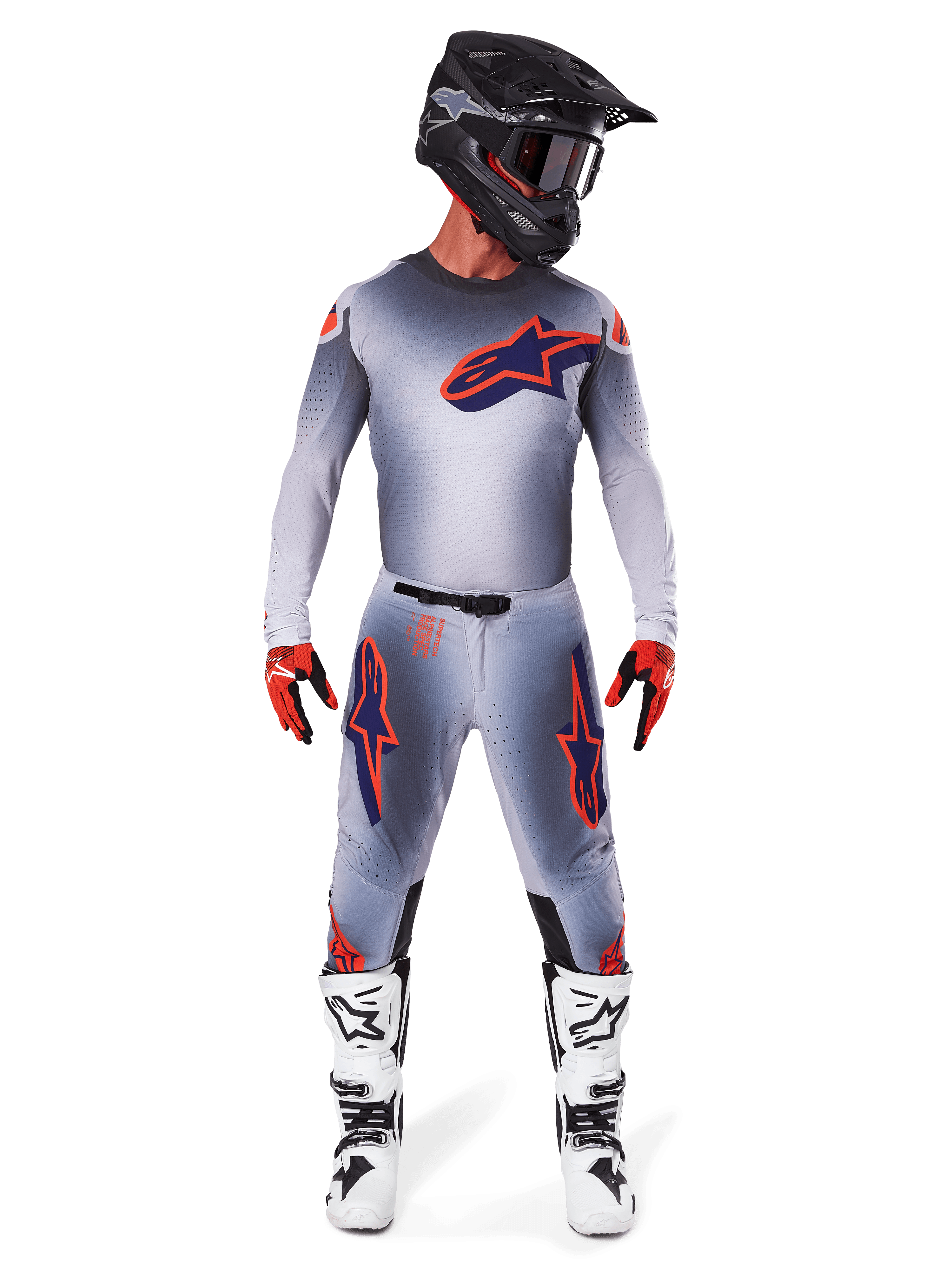 Zawodnik motocrossowy w koszulce Alpinestars 2025 Supertech Lipan w kolorze Gray Orange Fluo, szary gradient i pomarańczowe logo, w zestawie z dopasowanymi spodniami motocrossowymi, czarnym kaskiem, białymi butami i pomarańczowymi rękawicami, profesjonalny zestaw wyścigowy.