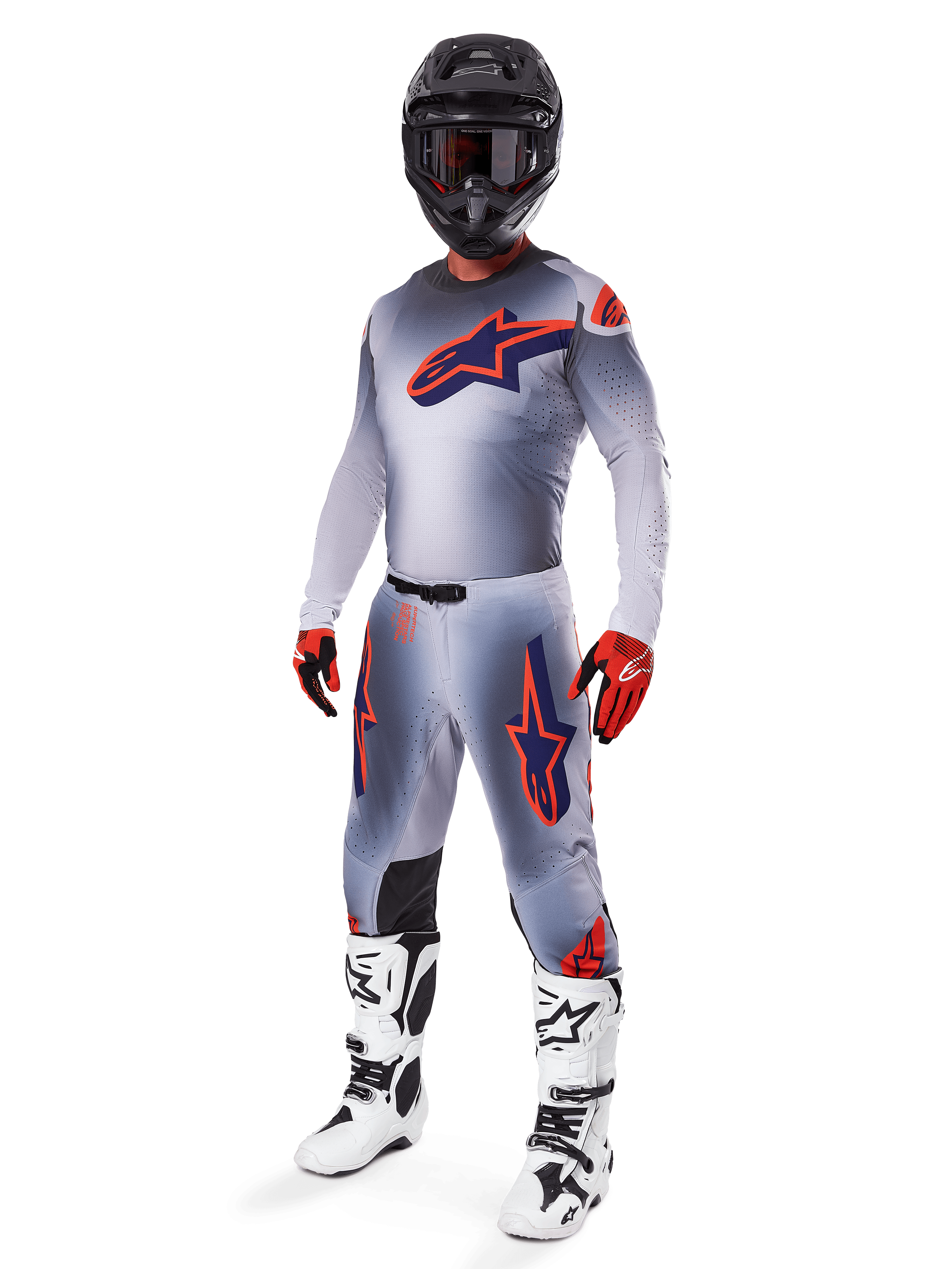 Zawodnik motocrossowy ubrany w koszulkę Alpinestars Supertech Lipan 2025 w kolorze szarym i pomarańczowym fluo, pasujące szare spodnie z pomarańczowymi akcentami, czarny kask, biało-czarne buty oraz pomarańczowo-czarne rękawice, profesjonalny zestaw odzieży do wyścigów terenowych