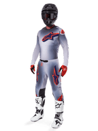 Zestaw motocrossowy Alpinestars Supertech Lipan 2025, szary z grafikami gwiazd w kolorach pomarańczowym fluo i granatowym, czarny kask, czerwono-czarne rękawice i biało-czarne buty, kompletny profesjonalny strój terenowy o wentylowanej konstrukcji