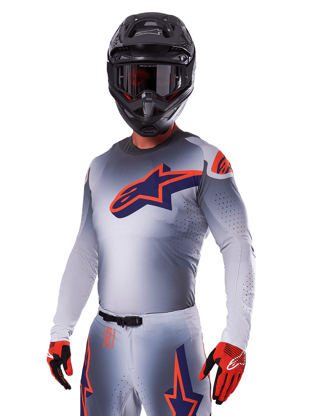 Motocyklista motocrossowy w zestawie Alpinestars 2025 Supertech Lipan, szara koszulka i spodnie z granatowymi i pomarańczowymi akcentami, matowy czarny kask z goglami oraz czerwono-czarne rękawice, sportowa odzież wyczynowa do wyścigów terenowych