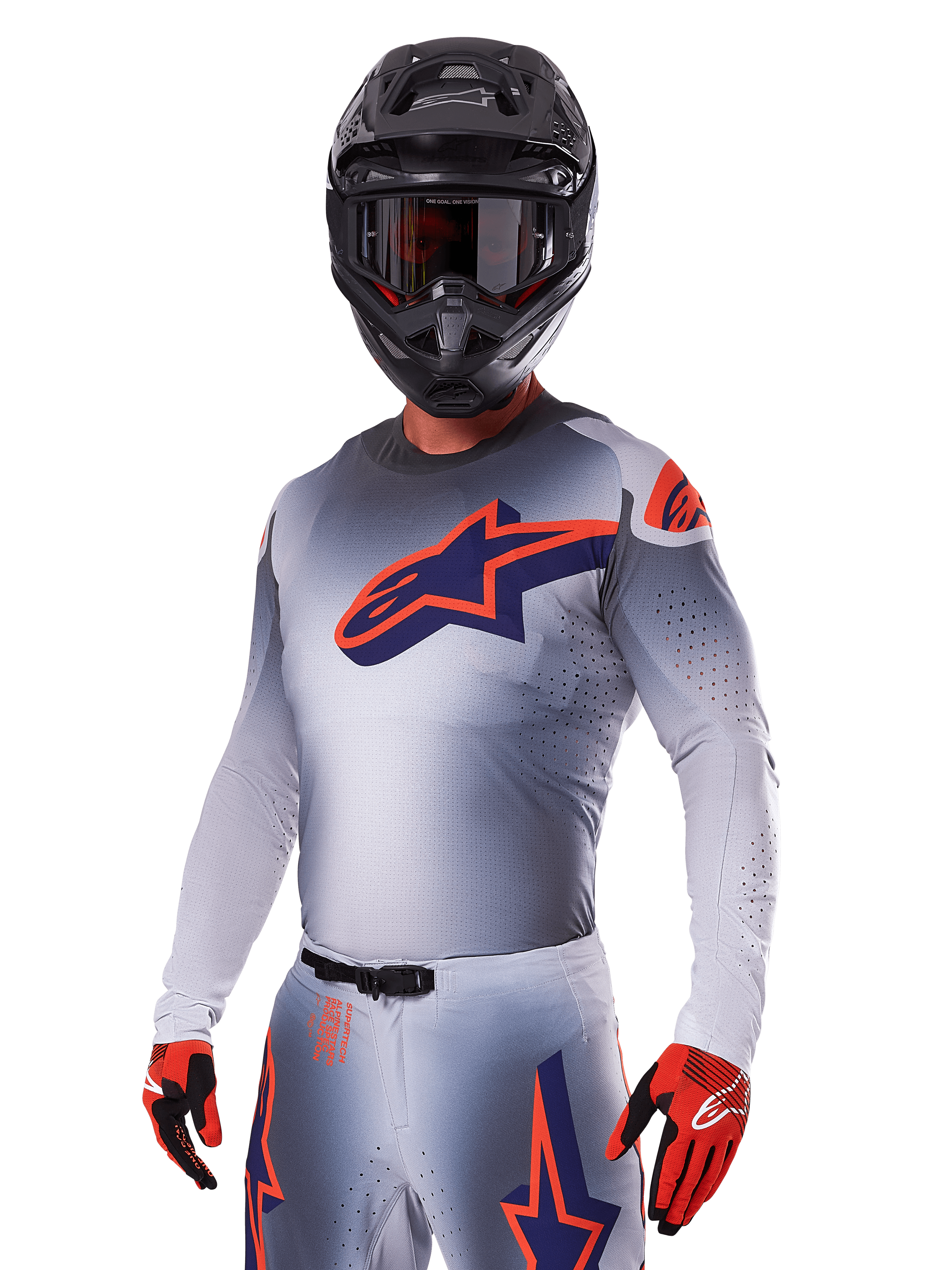 Motocyklista motocrossowy w zestawie Alpinestars 2025 Supertech Lipan, szara koszulka i spodnie z granatowymi i pomarańczowymi akcentami, matowy czarny kask z goglami oraz czerwono-czarne rękawice, sportowa odzież wyczynowa do wyścigów terenowych