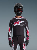 Alpinestars 2026 Supertech AFD Vista Jersey, koszulka motocrossowa w kolorach czarnym, czerwonym i białym, widoczna na motocykliście w czarnym kasku, goglach i rękawicach, z dużym logo na piersi i brandingiem „SUPERTECH AFD”, profesjonalna odzież wyścigowa do jazdy terenowej