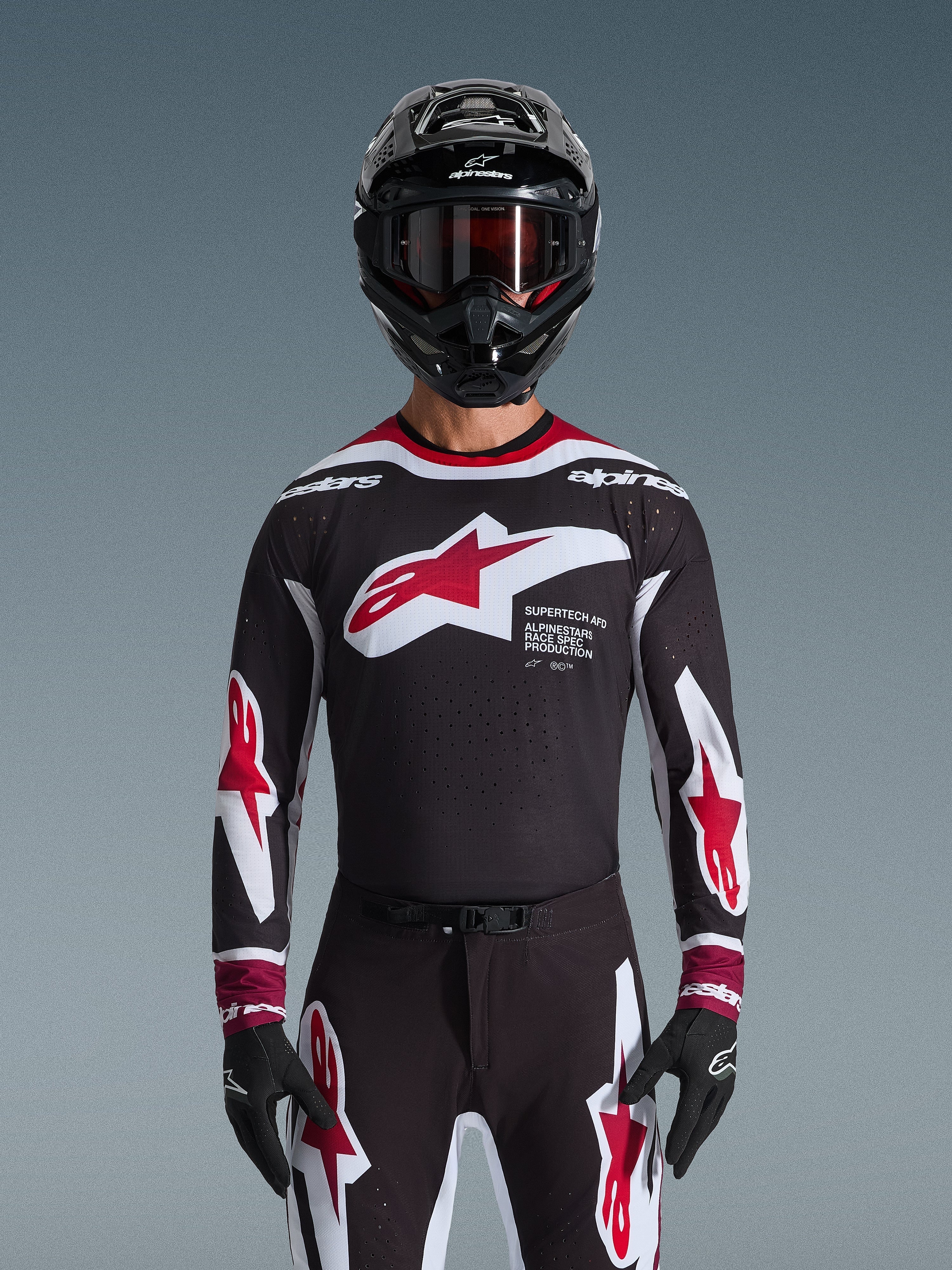 Alpinestars 2026 Supertech AFD Vista Jersey, koszulka motocrossowa w kolorach czarnym, czerwonym i białym, widoczna na motocykliście w czarnym kasku, goglach i rękawicach, z dużym logo na piersi i brandingiem „SUPERTECH AFD”, profesjonalna odzież wyścigowa do jazdy terenowej