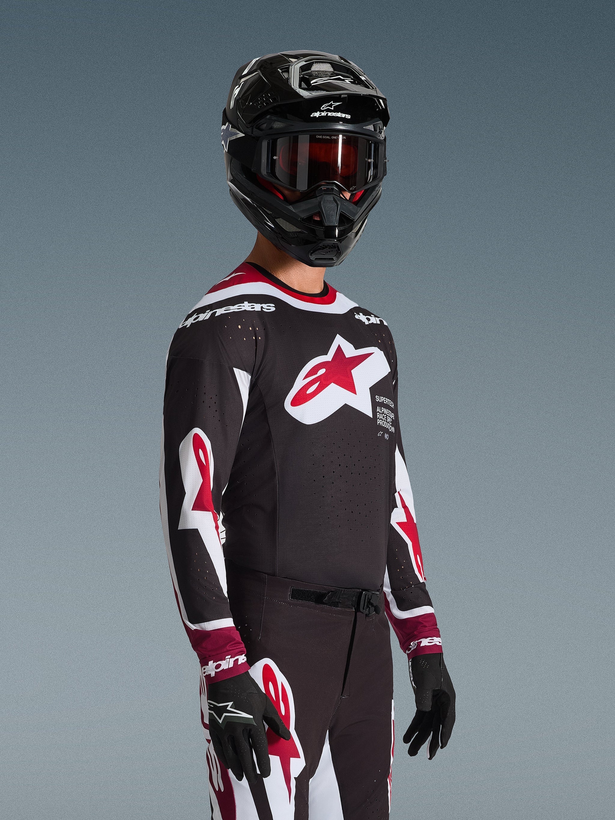 Motocyklista motocrossowy ubrany w koszulkę Alpinestars 2026 Supertech AFD Vista w kolorze czarno-czerwono-białym, z dużym czerwonym logo gwiazdy na piersi i laserowo wycinanymi perforacjami, w połączeniu z czarnym kaskiem i dopasowanymi spodniami wyścigowymi.