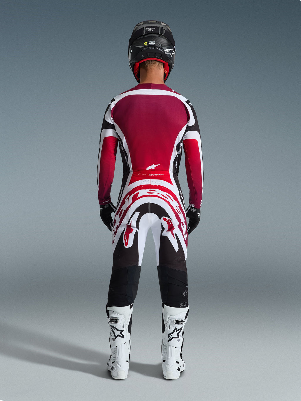 Alpinestars 2026 Supertech AFD Vista Gear Set, Rear view of a motocross rider in professional racing gear, burgundy and red jersey with white and black accents, matching pants with bold graphics, white boots, and black helmet, coordinated motocross racing outfit.