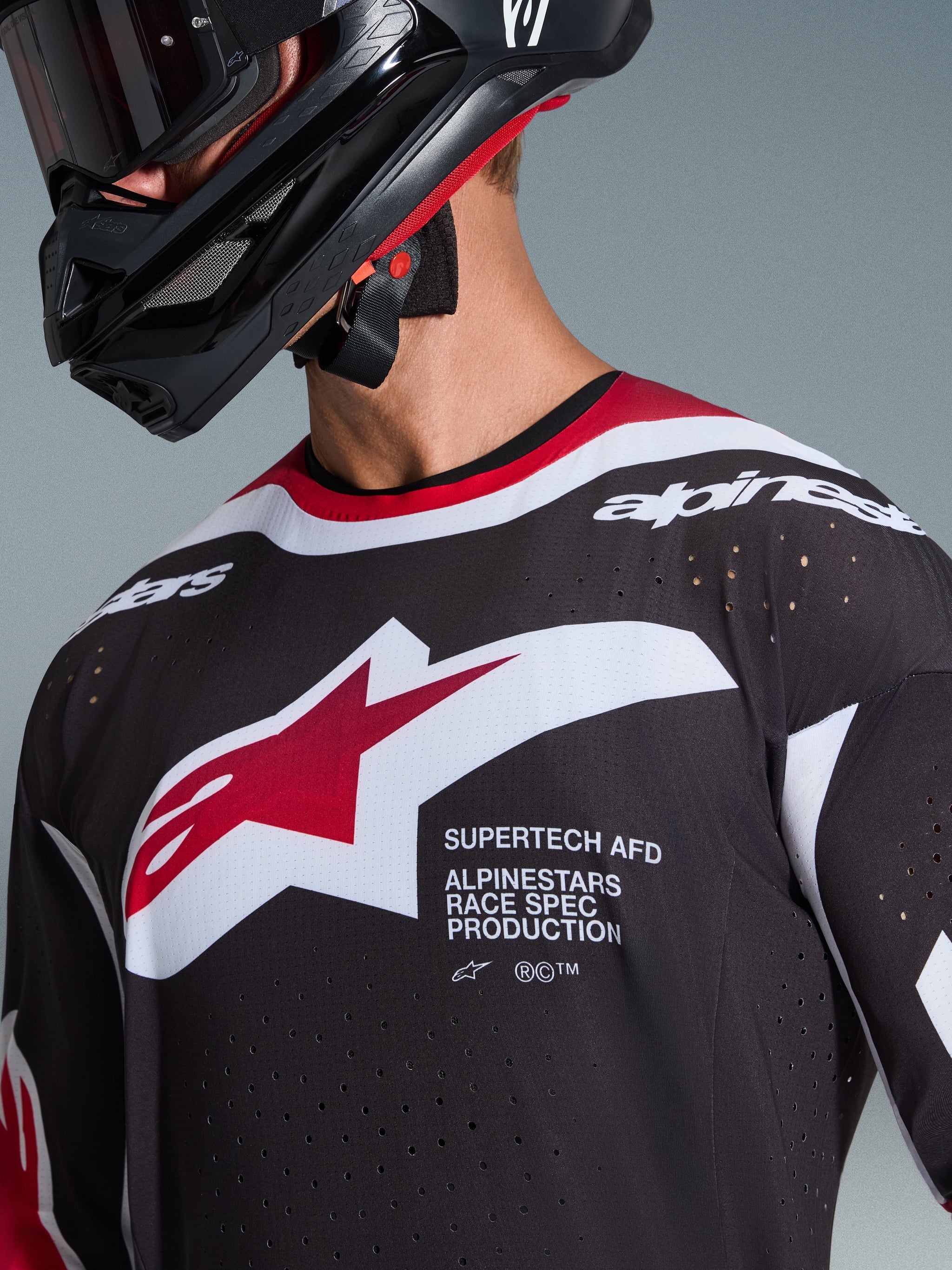 Alpinestars 2026 Supertech AFD Vista Jersey, zbliżenie na motocyklistę motocrossowego, czarna koszulka z czerwonymi i białymi akcentami, duże biało-czerwone logo Alpinestars, laserowo wycinane perforacje wentylacyjne, profesjonalny krój wyścigowy, czarny kask