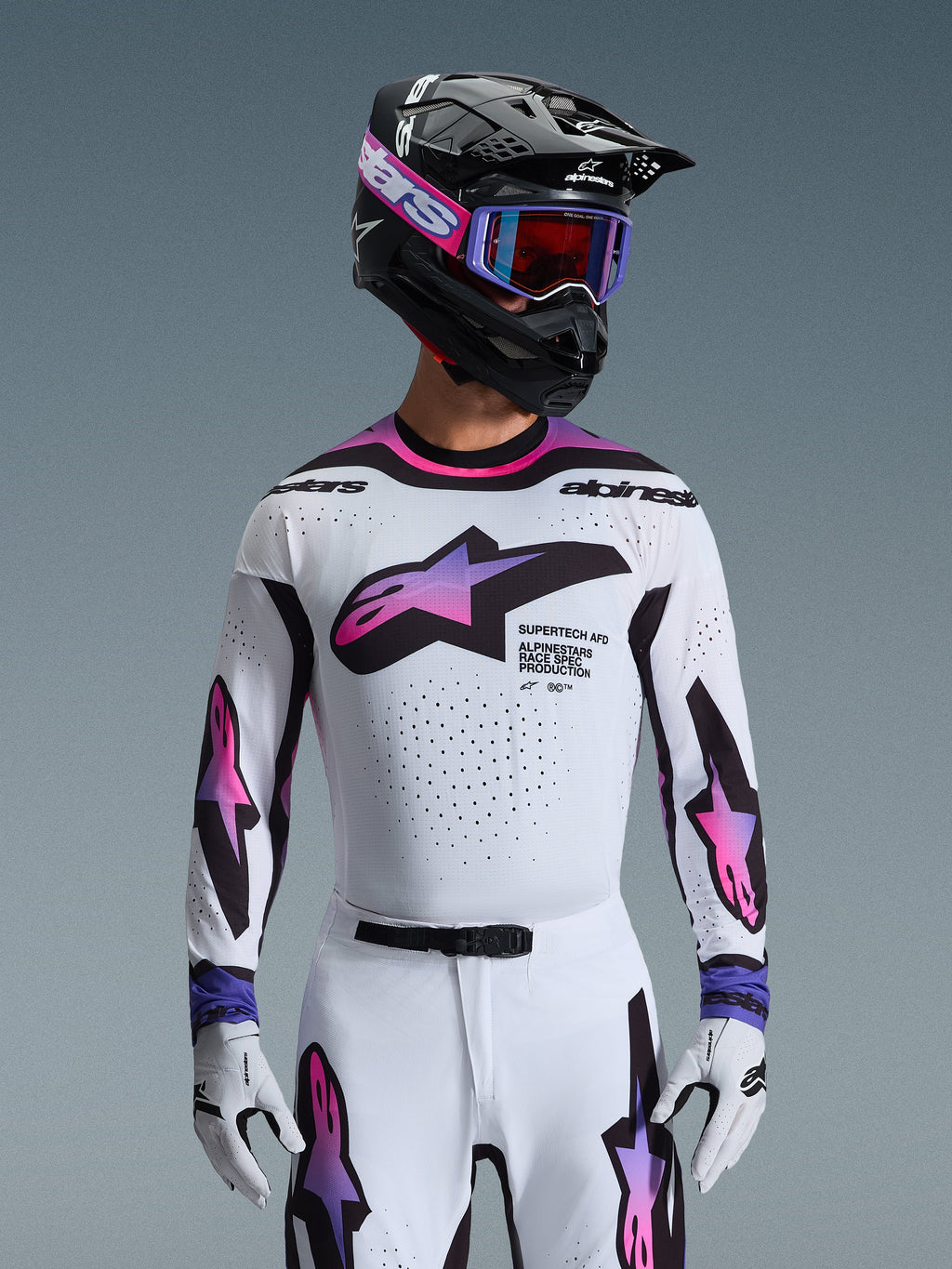 Alpinestars 2026 Supertech AFD Vista Gear Set, profesjonalny strój motocrossowy, biała koszulka i spodnie z różowo-fioletową grafiką gradientową, czarny kask z fioletowymi goglami i białe rękawice, sportowy krój wyścigowy do jazdy terenowej.