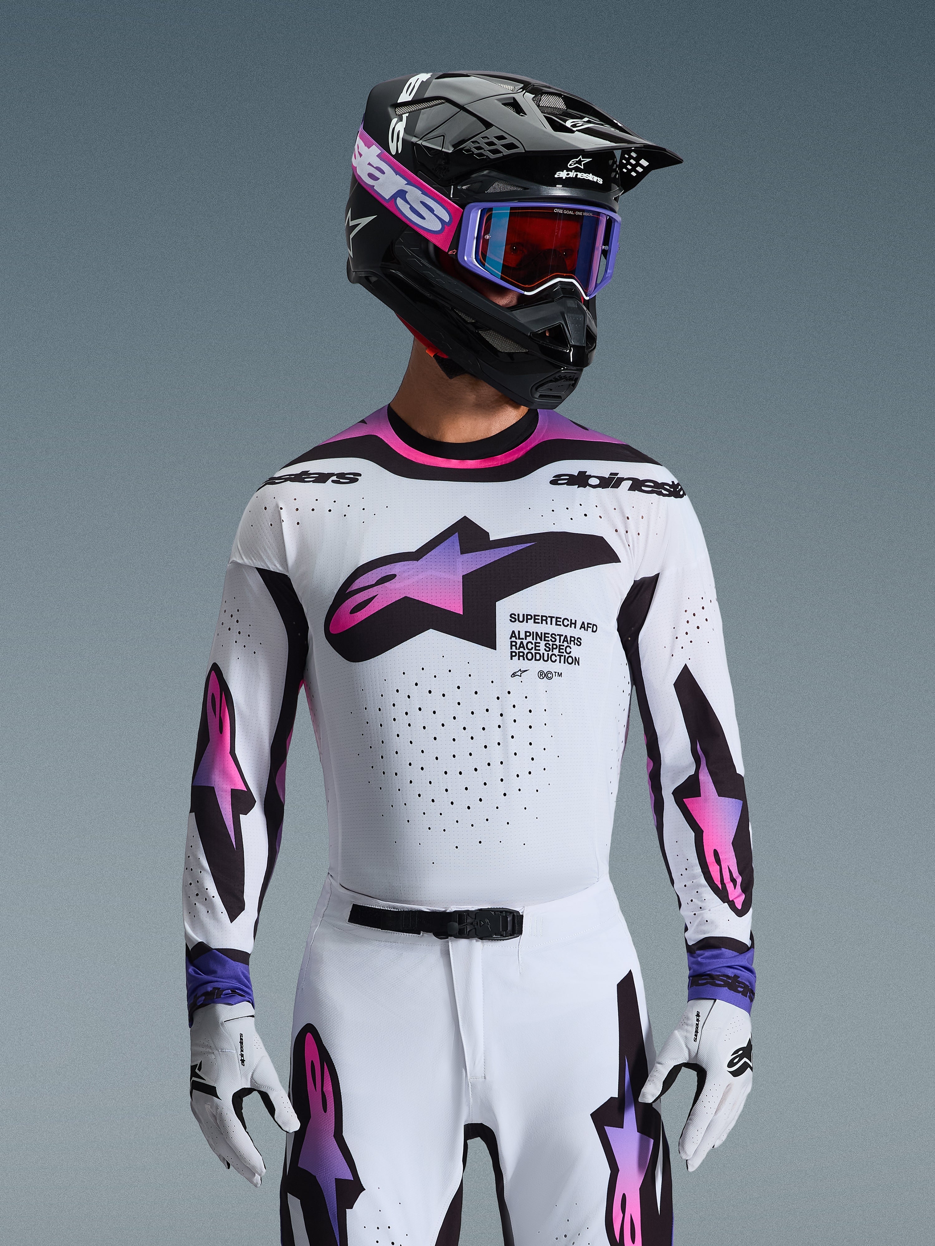 Alpinestars 2026 Supertech AFD Vista Gear Set, profesjonalny strój motocrossowy, biała koszulka i spodnie z różowo-fioletową grafiką gradientową, czarny kask z fioletowymi goglami i białe rękawice, sportowy krój wyścigowy do jazdy terenowej.