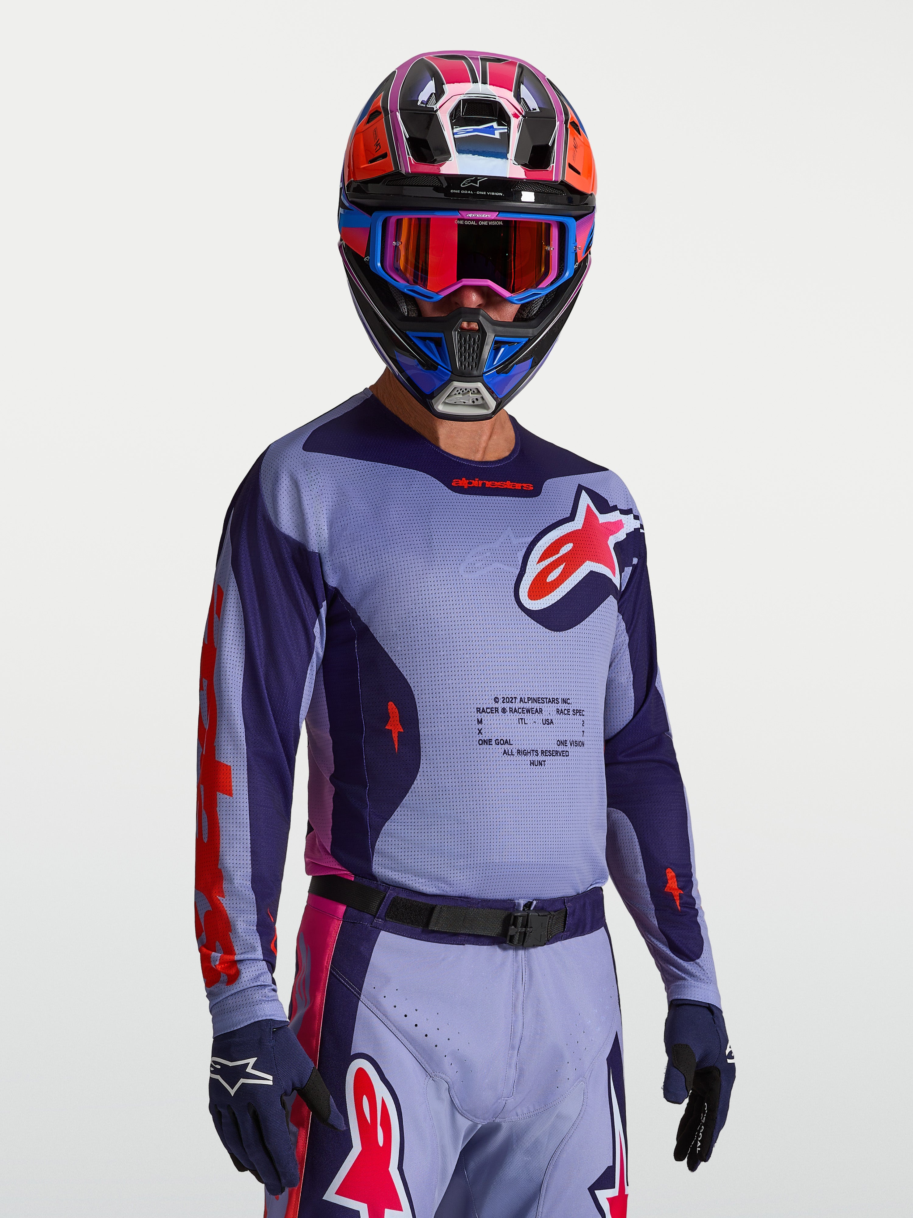Alpinestars Koszulka Racer Air Hunt, męska koszulka motocrossowa, fioletowa i różowa, przewiewna konstrukcja z pełnej siatki, idealna do jazdy off-road, prezentowana na modelu w kasku i rękawicach.