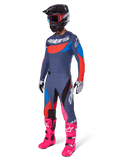 Alpinestars Techstar Dreem 2025, kompletny zestaw motocrossowy, strój wyścigowy off-road z szaro-niebieską koszulką z czerwonymi akcentami, pasujące spodnie z różowymi elementami, czarny kask, jaskraworóżowe buty oraz biało-czarne rękawice