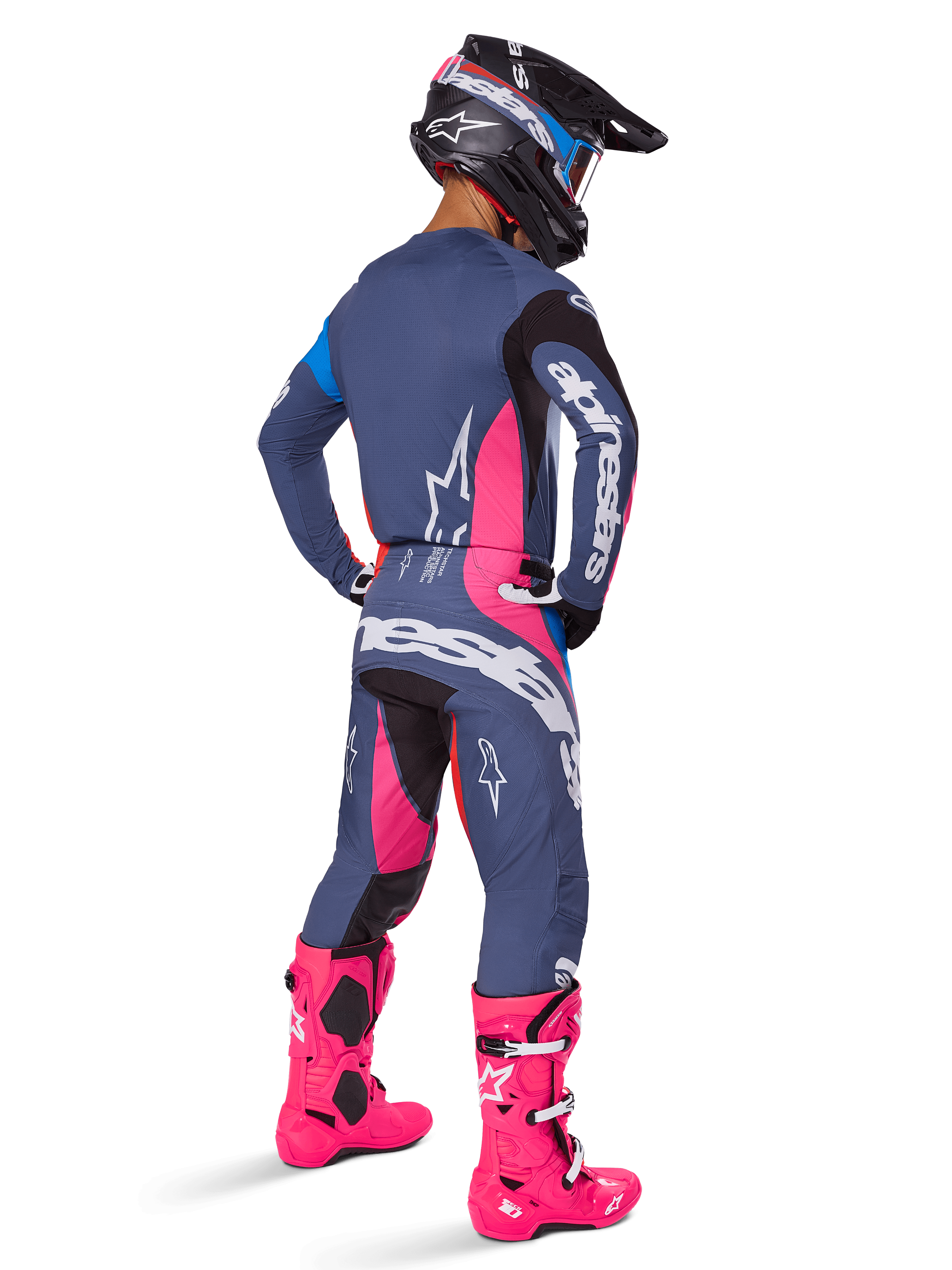 Zawodnik motocrossowy widoczny z tyłu, ubrany w zestaw odzieży Alpinestars 2025 Techstar Dreem, szary z jaskraworóżowymi i białymi akcentami, czarno-biały kask i jaskraworóżowe buty, kompletny strój wyścigowy do motocrossu.