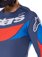 Zbliżenie na koszulkę Alpinestars 2025 Techstar Dreem, granatowa z jaskrawymi niebieskimi i pomarańczowymi akcentami, białe logo Alpinestars na klatce piersiowej i ramieniu, widoczne laserowo wycinane perforacje dla wentylacji