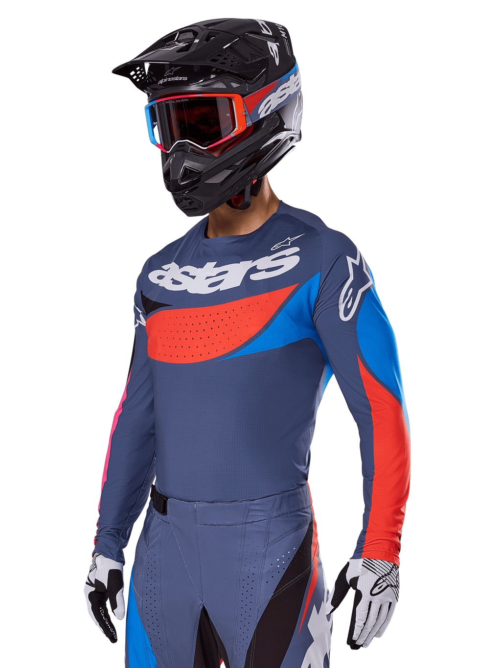 Alpinestars 2025 Techstar Dreem Gear Set, motocyklista motocrossowy w szaroniebieskiej koszulce i spodniach z wyrazistymi czerwonymi i niebieskimi grafikami, logo „astars” na klatce piersiowej, czarny kask, gogle z czerwonymi oprawkami i białe rękawice wyścigowe