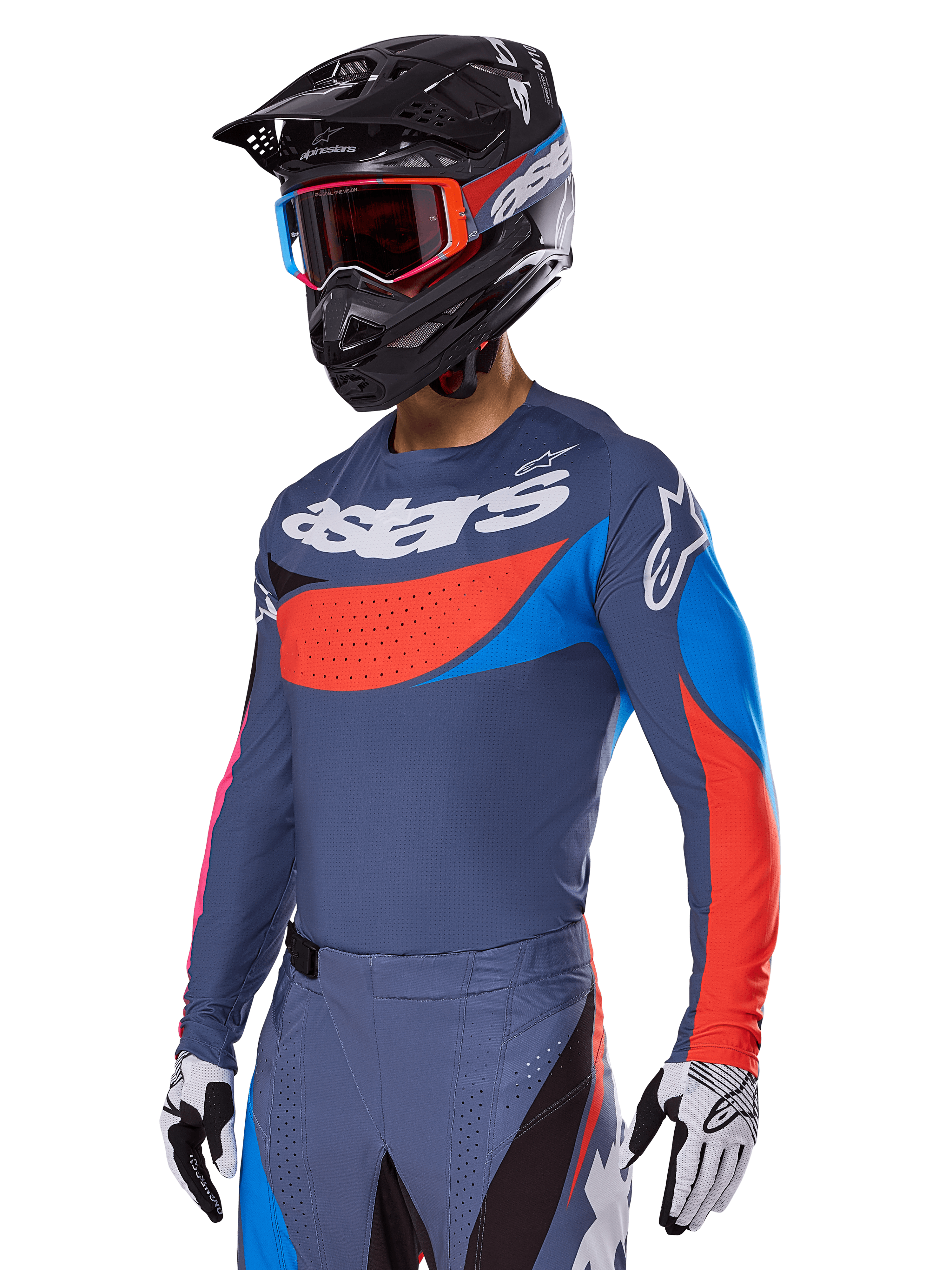 Alpinestars 2025 Techstar Dreem Gear Set, motocyklista motocrossowy w szaroniebieskiej koszulce i spodniach z wyrazistymi czerwonymi i niebieskimi grafikami, logo „astars” na klatce piersiowej, czarny kask, gogle z czerwonymi oprawkami i białe rękawice wyścigowe