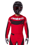 Alpinestars Techstar Dreem Jersey 2025, koszulka motocrossowa, jasnoczerwona i czarna, białe logo „astars”, czarny wentylowany panel na klatce piersiowej, kompletny strój ze spodniami, czarnym kaskiem i biało-czarnymi rękawicami