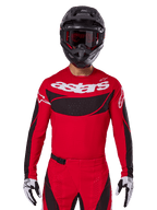 Alpinestars Techstar Dreem Jersey 2025, koszulka motocrossowa, jasnoczerwona i czarna, białe logo „astars”, czarny wentylowany panel na klatce piersiowej, kompletny strój ze spodniami, czarnym kaskiem i biało-czarnymi rękawicami
