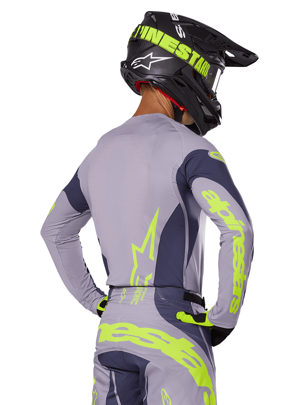 Zawodnik motocrossowy widoczny od tyłu w zestawie Alpinestars 2025 Techstar Dreem, szara koszulka i spodnie z jaskrawym neonowym żółto-zielonym brandingiem, pasujący czarny kask z neonową grafiką, profesjonalny strój wyścigowy