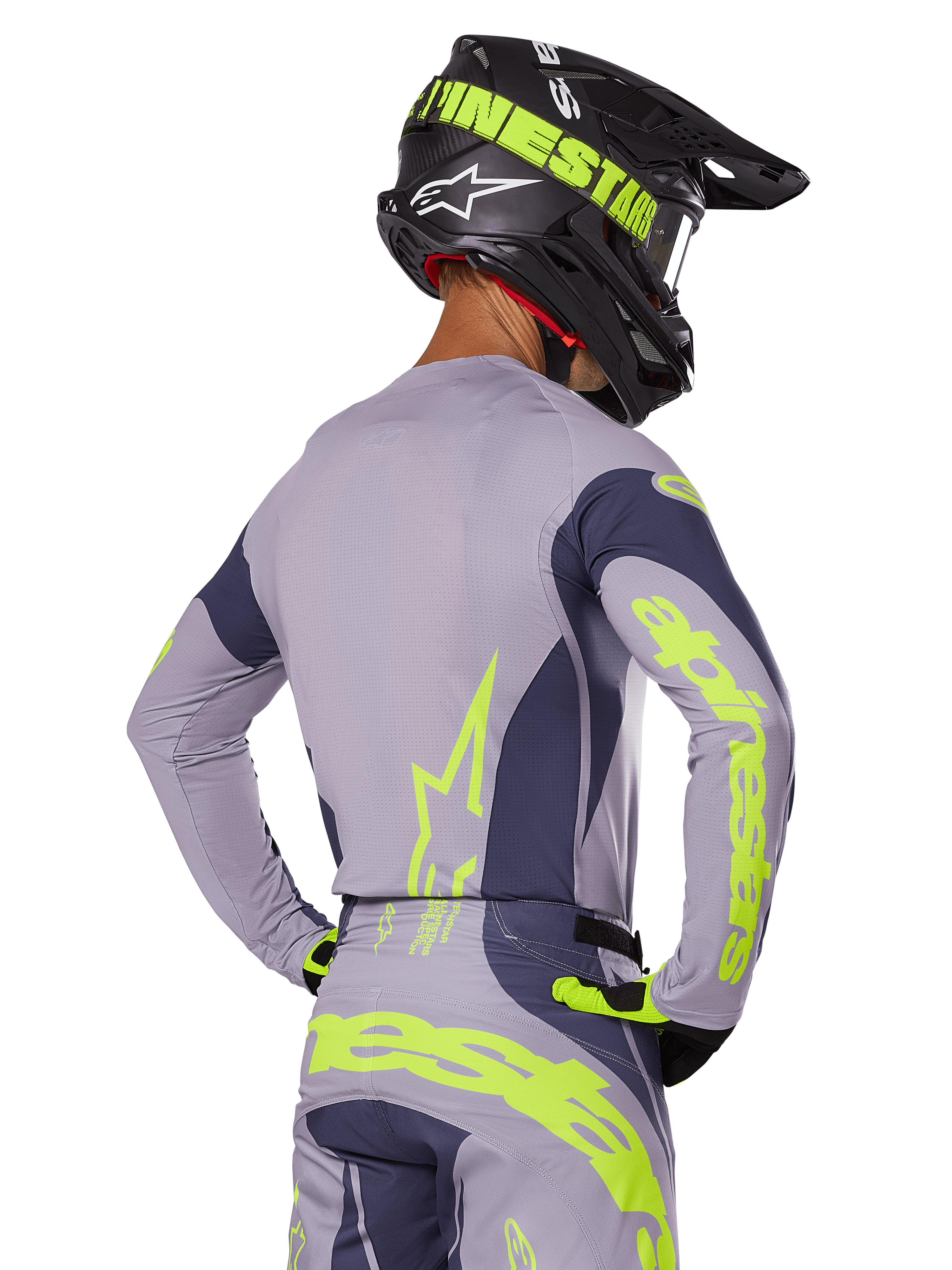 Zawodnik motocrossowy widoczny od tyłu w zestawie Alpinestars 2025 Techstar Dreem, szara koszulka i spodnie z jaskrawym neonowym żółto-zielonym brandingiem, pasujący czarny kask z neonową grafiką, profesjonalny strój wyścigowy