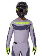 Alpinestars Techstar Dreem Jersey i zestaw odzieży 2025, strój motocrossowy, jasnoszary i ciemnoszary z neonowożółtymi akcentami, z logo „astars”, noszony z czarnym kaskiem, goglami i dopasowanymi rękawicami, techniczny perforowany materiał zapewniający wydajność w terenie