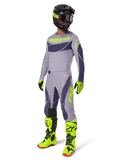 Zestaw Alpinestars 2025 Techstar Dreem, zawodnik motocrossowy w pełnym stroju wyścigowym, szara koszulka i spodnie z ciemnoszarymi wzorami i neonowymi żółto-zielonymi akcentami, dopasowany czarny kask, neonowe żółto-zielone rękawice i buty, wyczynowa odzież off-road