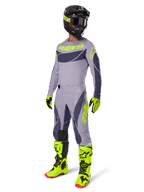 Zestaw Alpinestars 2025 Techstar Dreem, zawodnik motocrossowy w pełnym stroju wyścigowym, szara koszulka i spodnie z ciemnoszarymi wzorami i neonowymi żółto-zielonymi akcentami, dopasowany czarny kask, neonowe żółto-zielone rękawice i buty, wyczynowa odzież off-road