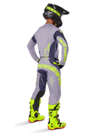Koszulka Alpinestars Techstar Dreem 2025, koszulka motocrossowa, szara i ciemnoszara, noszona z dopasowanymi spodniami i jaskrawymi, neonowożółtymi butami, widok z tyłu ukazujący neonowożółte logo oraz sportowy krój do wyścigów terenowych