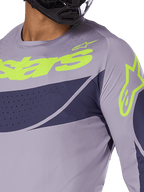 Alpinestars Techstar Dreem Jersey 2025, koszulka motocrossowa, szaro-granatowa z jaskrawym limonkowym logo, zbliżenie na motocyklistę w czarnym kasku, z laserowo wycinanymi perforacjami zapewniającymi wentylację
