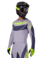 Motocyklista motocrossowy w koszulce Alpinestars 2025 Techstar Dreem, szary i ciemnoszary z limonkowymi logo, pasujące spodnie, czarny kask z limonkowymi akcentami, limonkowo-czarne rękawice, skoordynowany strój do wyścigów terenowych