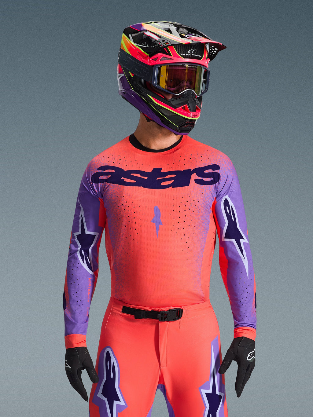 Alpinestars Supertech Scenz Jersey 2026, koszulka motocrossowa, koralowa i fioletowa, z dużym logo „astars” i wzorami gwiazd na rękawach, noszona z dopasowanymi spodniami i wielokolorowym kaskiem, zaawansowana odzież terenowa
