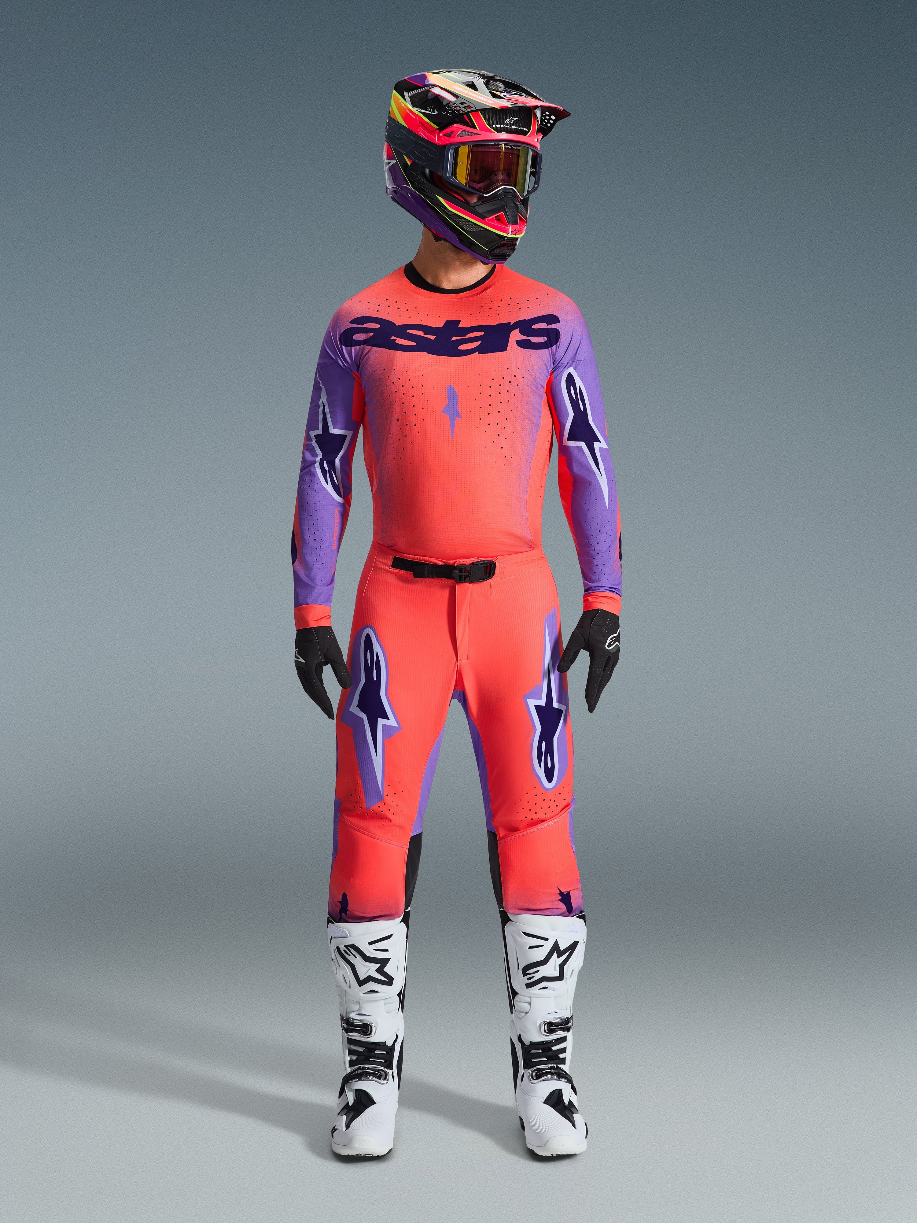 Zestaw odzieży Supertech Scenz 2026, strój motocrossowy Alpinestars, intensywny czerwono-pomarańczowy i fioletowy, koszulka z czarnym brandingiem „astars”, pasujące spodnie z fioletowymi logotypami gwiazd, kolorowy kask wyścigowy i białe buty, profesjonalny zestaw wyczynowy off-road