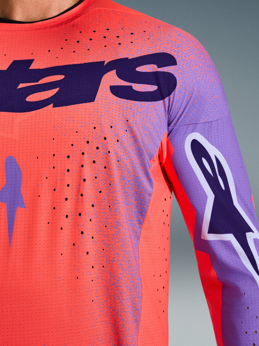 Alpinestars 2026 Supertech Scenz Jersey, koszulka motocrossowa, kolor koralowy i fioletowy, zbliżenie pokazujące teksturę oddychającej siatki i perforacje wycinane laserowo, z dużym fioletowym logo na piersi i grafikami na rękawach, do profesjonalnych wyścigów terenowych