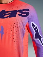 Alpinestars 2026 Supertech Scenz Jersey, koszulka motocrossowa, kolor koralowy i fioletowy, zbliżenie pokazujące teksturę oddychającej siatki i perforacje wycinane laserowo, z dużym fioletowym logo na piersi i grafikami na rękawach, do profesjonalnych wyścigów terenowych