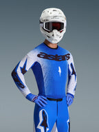 Koszulka Alpinestars Supertech Scenz 2026, koszulka motocrossowa, niebiesko-biała, kompletny zestaw z dopasowanymi niebieskimi spodniami i rękawicami, czarny branding „astars”, biały kask i ciemne gogle, profesjonalny sportowy krój wyścigowy.