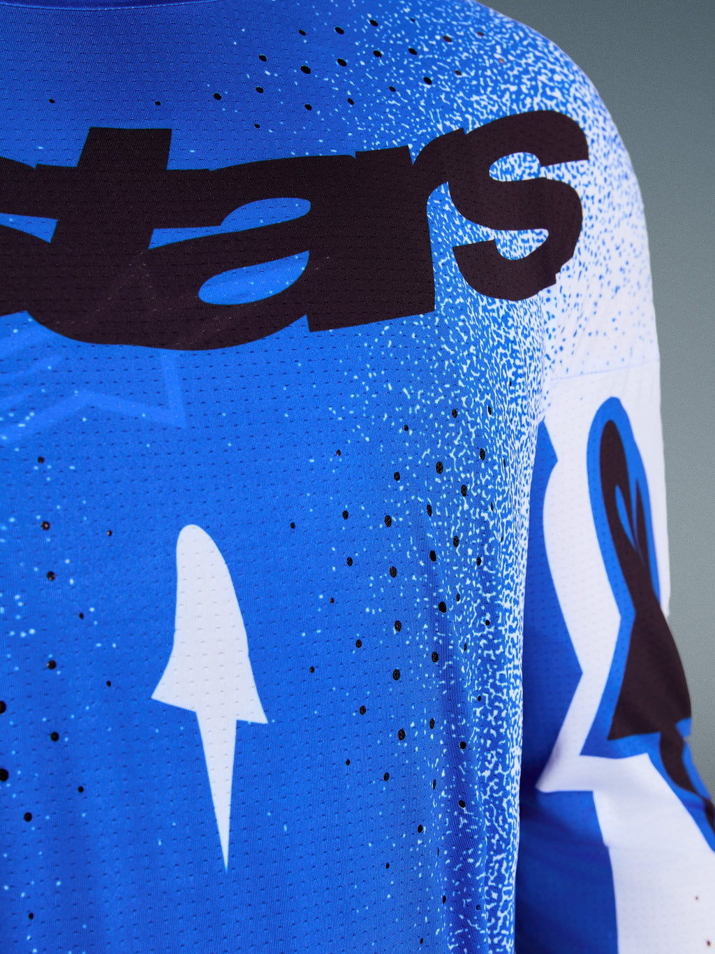 Alpinestars Supertech Scenz Jersey 2026, zbliżenie na niebiesko-biały design (Ucla Blue), laserowo wycinane perforacje dla lepszej wentylacji, czarny branding „stars” oraz oddychający materiał typu mesh do profesjonalnych wyścigów motocrossowych.