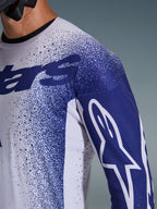 Alpinestars 2026 Supertech Scenz Jersey, zbliżenie na koszulkę w kolorze jasnoszarym i ciemnoniebieskim, laserowo wycinane perforacje, nakrapiany wzór graficzny, białe logo Astars na rękawie, profesjonalny krój motocrossowy