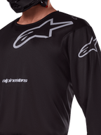 Alpinestars 2025 Racer Graphite Jersey, czarno-szara, zbliżenie na motocyklistę w koszulce motocrossowej, szare logo Alpinestars i gwiazdy A-star, techniczny materiał poliestrowy do jazdy terenowej