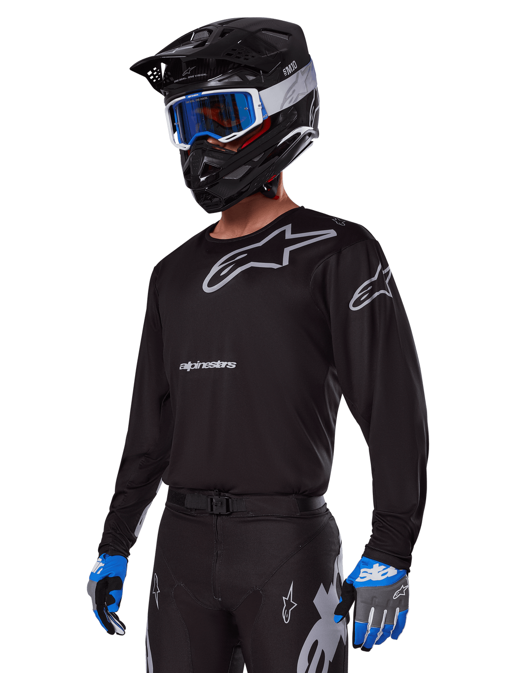 Zawodnik motocrossowy w zestawie Alpinestars 2025 Racer Graphite, czarna koszulka z szarymi logotypami Alpinestars, pasujące czarne spodnie z szarymi akcentami, czarny kask z niebiesko-białymi goglami, niebiesko-szare rękawice, nowoczesny strój techniczny do jazdy off-road