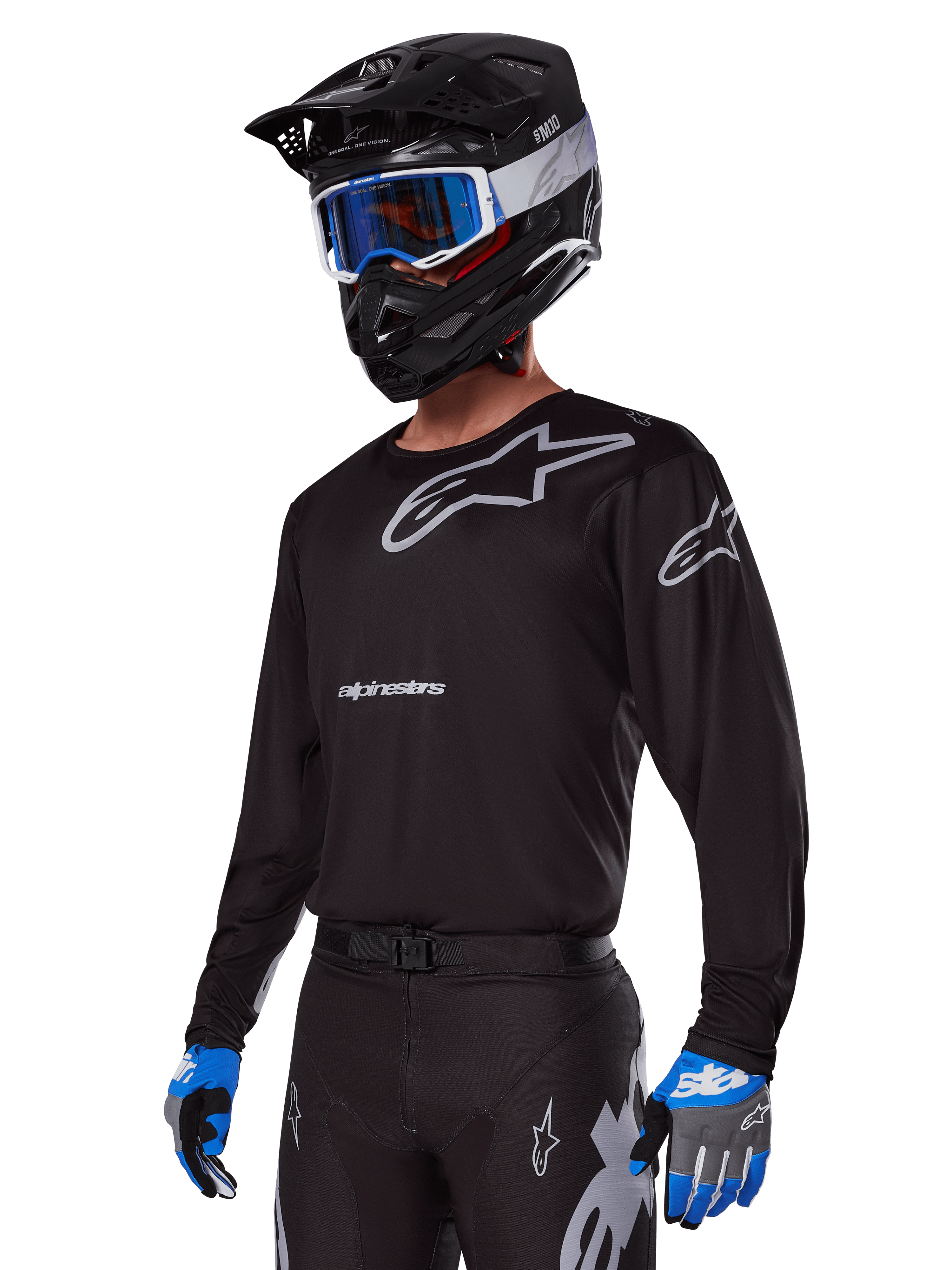 Zawodnik motocrossowy w zestawie Alpinestars 2025 Racer Graphite, czarna koszulka z szarymi logotypami Alpinestars, pasujące czarne spodnie z szarymi akcentami, czarny kask z niebiesko-białymi goglami, niebiesko-szare rękawice, nowoczesny strój techniczny do jazdy off-road
